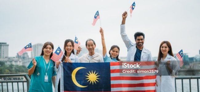 Group portrait of medical staff holding the Malaysian flag at a public park, celebrating Independence Day and National Day.